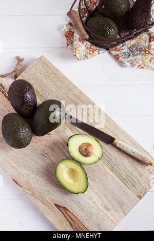 Ganze und eine halbierte Avocados avocado auf einem Holzbrett (von oben gesehen) Stockfoto