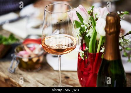 Ein Glas Champagner Rosé, ein Bündel von Frühling Blumen und eine Flasche Champagner auf einer hölzernen Tisch Stockfoto