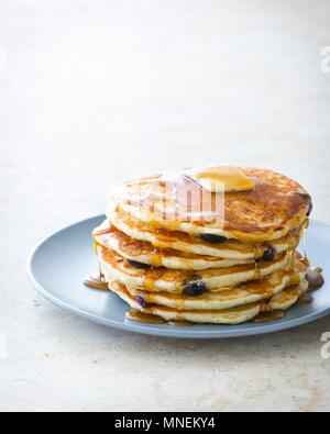 Ein Stapel von blaubeerpfannkuchen auf einem Teller mit Ahornsirup und Butter Stockfoto