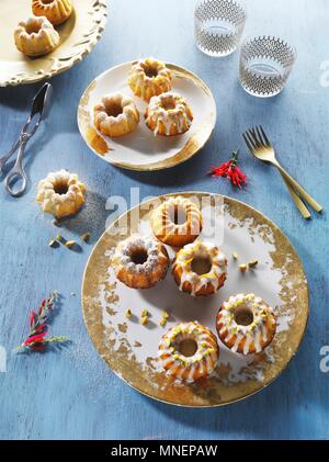 Mini Bundt Kuchen auf Gold-gemusterten Platten auf einem blauen Holz- Oberfläche Stockfoto