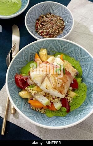 Cod eingewickelt in Speck auf einem Bett von Gemüse und Couscous mit grüner Soße Stockfoto