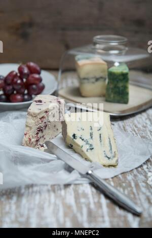 Cambozola und Wensleydale Käse auf ein Stück Papier mit einer Käseplatte und Trauben im Hintergrund Stockfoto