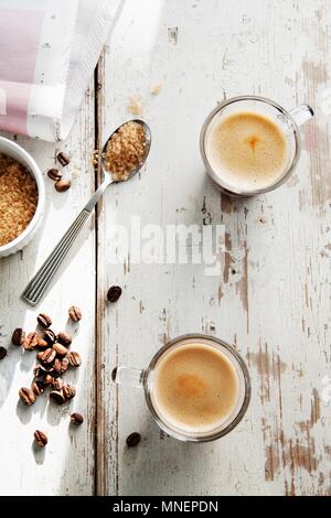 Kaffeebohnen, ein Teelöffel braunen Zucker und zwei Tassen Espresso auf einem weiß getünchten Tischplatte Stockfoto