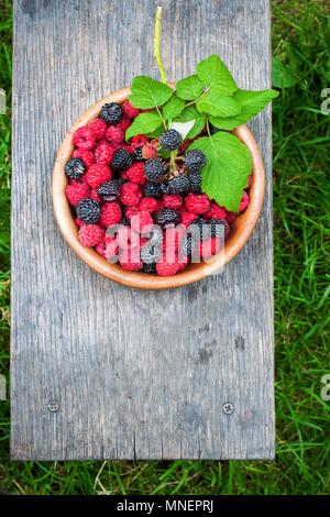 Frische Himbeeren und Brombeeren in einer Schüssel auf einem Holzbrett Stockfoto