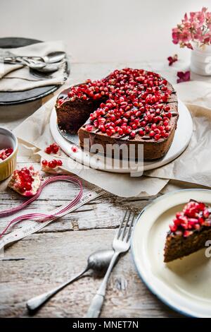 Schokoladenkuchen in der Form eines Herzens mit Schokoladenüberzug und Granatapfel Samen Stockfoto