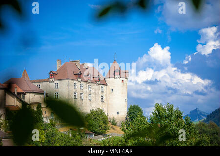 Blick durch die Bäume zu Gruyeres Schloss (Chateau de Gruyeres), in die Voralpen der Schweiz. Grünen Wipfel, blauer Himmel und die Berge in der Ferne Stockfoto