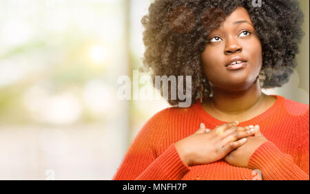 Schöne afrikanische Frau mit charmanten Lächeln, Hände auf Herz, Liebe und Mitgefühl zu zeigen, Außenpool Stockfoto