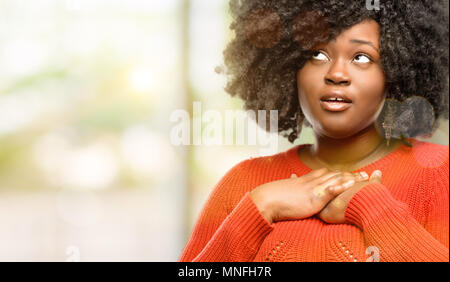 Schöne afrikanische Frau mit charmanten Lächeln, Hände auf Herz, Liebe und Mitgefühl zu zeigen, Außenpool Stockfoto