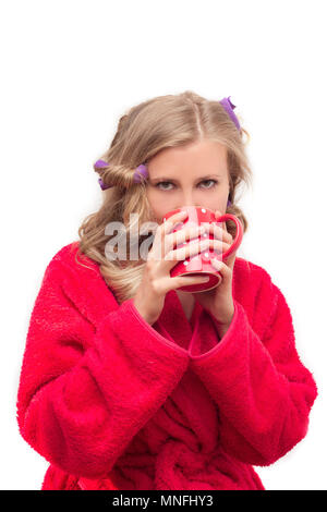 Mädchen in einer roten Robe und Lockenwickler trinken Tee am Morgen Stockfoto