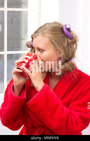 Mädchen in einer roten Robe und Lockenwickler trinken Tee am Morgen Stockfoto