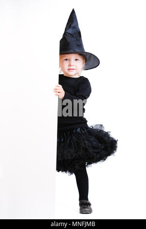 Verspielte kleine Mädchen Kleider für Halloween in Hexe Kostüm versteckt sich hinter weißen Banner Stockfoto