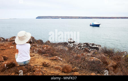 Kleines Mädchen sitzt auf einem Kliff von North Seymour Insel auf Galapagos und herrlicher Aussicht Stockfoto