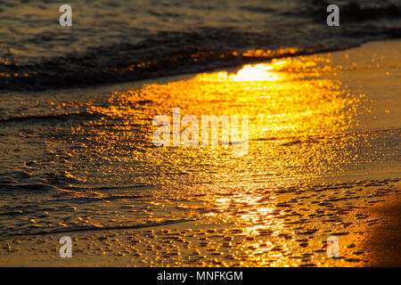 Schöne bunte Formen durch brechende Wellen auf einem Sandstrand und Sonne Reflexionen bei Sonnenuntergang erstellt Stockfoto