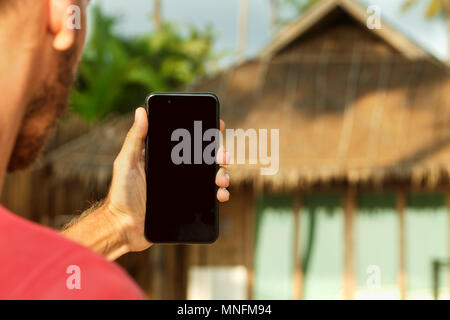 Mobile Anwendung für Reisen, Mann, Hand, smart phone mit schwarzen Bildschirm am Strand. Buchung und Reservierung Konzept mit Kopie Raum Stockfoto