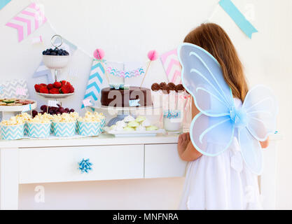 Adorable kleine Fee Mädchen mit Flügeln auf einer Geburtstagsfeier in der Nähe von Dessert Tabelle Stockfoto