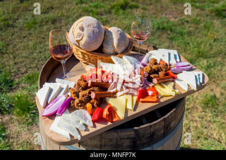 Erntesaison traditionelle rumänische Küche Teller mit Käse, Brot, Wurst, Zwiebeln und roter Wein im Glas in Weinbergen Stockfoto