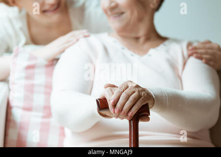 Ältere Frau ihre Hände, die mit lackierten Nägeln auf hölzernen Spazierstock Stockfoto