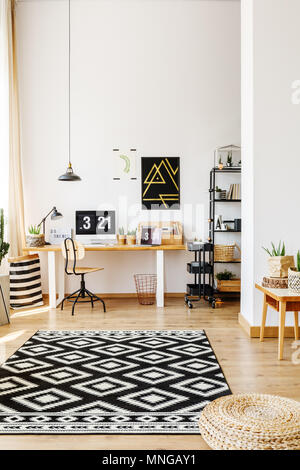 Moderne Atelier für kreative Hipster mit Schreibtisch, Computer, Speicher Warenkorb und gemusterten schwarze und weiße Wolldecke liegen auf Parkett Stockfoto