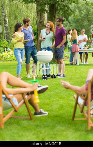 Freunde stand neben Grill, Menschen, die sich auf Liegestühlen Stockfoto