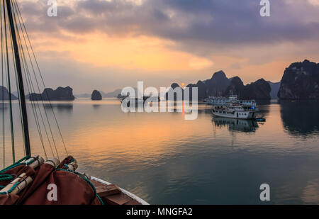 Einen schönen Sonnenaufgang unter den Kalkstein Inselchen und Kreuzfahrtschiffe in Ha Long Bay, ein UNESCO-Weltkulturerbe, in der Provinz Quang Ninh, Vietnam. Stockfoto