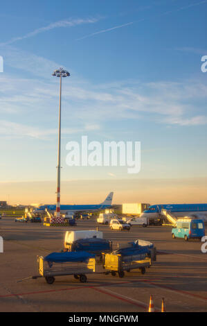 Die Schürze am Internationalen Flughafen Schiphol in Amsterdam, Niederlande, mit Flugzeug- und Gepäckwagen. Bei Sonnenuntergang aus einem Flugzeug fotografiert. Stockfoto