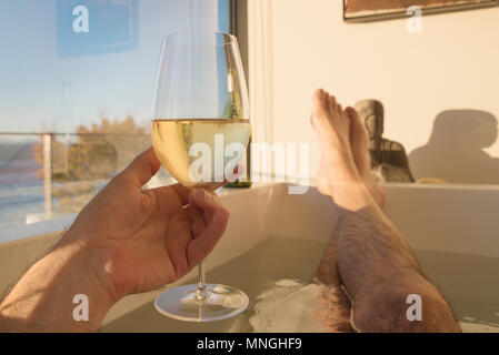 Sicht Mann entspannen in der Badewanne mit Meerblick am späten Nachmittag Sonne mit Glas Weisswein. Stockfoto