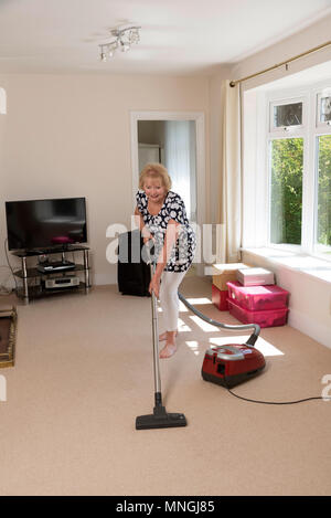 Home Umzüge, Frau mit einem Staubsauger den Teppich zu Hoover und das Bein dehnen Übungen Stockfoto
