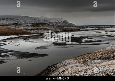 Smowy Wetter mit dunklen Wolke Himmel an einem Schwarzen geschliffen Riverbed in isländischer zurück Land bedeckt, April 2018 Stockfoto