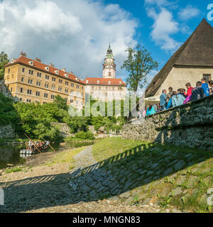 Rafting auf der Moldau in Cesky Krumlov mit seiner Burg, während die Leute im Freien in einer Bar/Restaurant gesellig sind. Tschechische Republik. Stockfoto