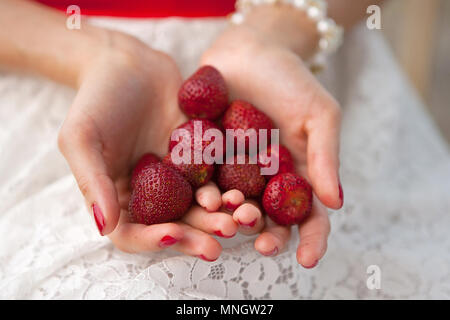 Weibliche Hände halten eine Handvoll roten Erdbeeren ohne Blätter. Beeren pflücken im Sommer, demonstrieren die Ernte. Gesunde Ernährung, Vegetarismus Stockfoto