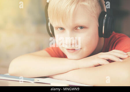 Blond kaukasischen Jungen in Kopfhörer ausruhen und das Hören von Musik in einer Pause zwischen seine Hausaufgaben machen. Stockfoto