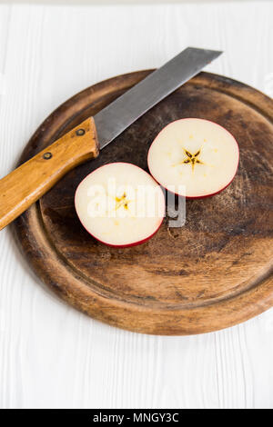 Close up in Scheiben geschnittenen roten Apfel mit Messer auf Schneidebrett und weiße Holztisch Stockfoto