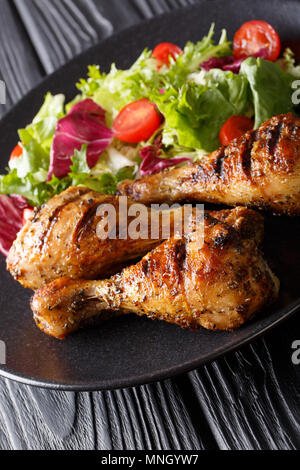 Knusprig gegrillte Hähnchenschenkel und frisches Gemüse Salat close-up auf einem Teller. Vertikale Stockfoto