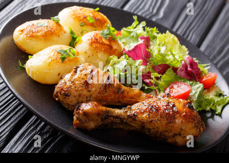 Portion gegrillte Hähnchenkeulen mit Kartoffeln und frischem Salat closeup auf einem Teller. Horizontale Stockfoto