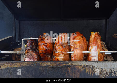 Schließen sich mehrere große Stücke von Schweinefleisch Schinken Fleisch gleichmässig gebraten auf offenen Holzfeuer Spieß, Betrachtungswinkel Stockfoto