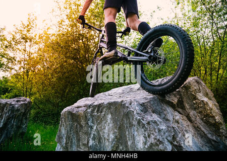 Radfahrer Beine auf einen Versuch mit dem Fahrrad oben auf einem Felsen bei Sonnenuntergang. Konzept der Extreme Sport Stockfoto