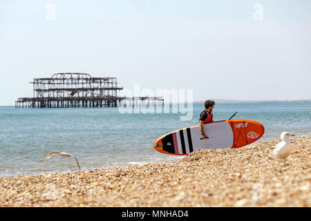 Ein Mann mit einem Surfbrett oder paddleboard verlassen das Meer während eines schönen Tages auf Brighton Seafront. Brighton, East Sussex, UK. Stockfoto