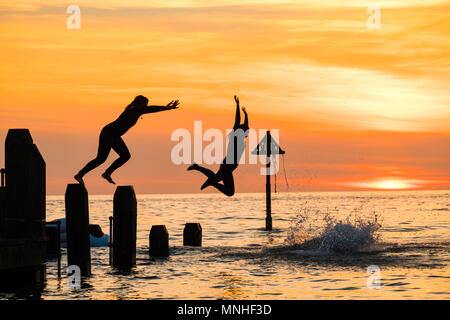 Aberystwyth Wales UK, Donnerstag, 17. Mai 2018 Deutschland Wetter: Bei Sonnenuntergang am Ende einer glorreichen Tag der warmen Frühlingssonne, eine Gruppe von Studenten sind wie Sie tauchen und springen Sie in das klare Wasser aus dem hölzernen Pier in Aberystwyth an der Westküste von Wales Foto © Keith Morris/Alamy Leben Nachrichten Silhouette Stockfoto