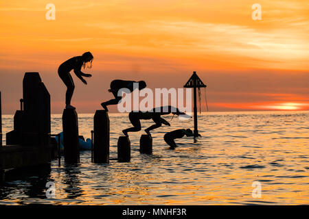 Aberystwyth Wales UK, Donnerstag, 17. Mai 2018 Deutschland Wetter: Bei Sonnenuntergang am Ende einer glorreichen Tag der warmen Frühlingssonne, eine Gruppe von Studenten sind wie Sie tauchen und springen Sie in das klare Wasser aus dem hölzernen Pier in Aberystwyth an der Westküste von Wales Foto © Keith Morris/Alamy Leben Nachrichten Silhouette Stockfoto