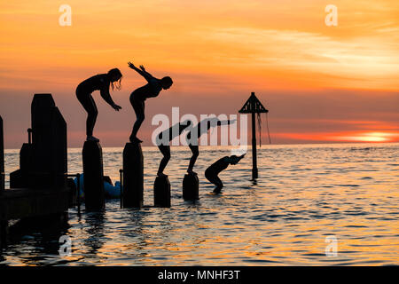 Aberystwyth Wales UK, Donnerstag, 17. Mai 2018 Deutschland Wetter: Bei Sonnenuntergang am Ende einer glorreichen Tag der warmen Frühlingssonne, eine Gruppe von Studenten sind wie Sie tauchen und springen Sie in das klare Wasser aus dem hölzernen Pier in Aberystwyth an der Westküste von Wales Foto © Keith Morris/Alamy Leben Nachrichten Silhouette Stockfoto