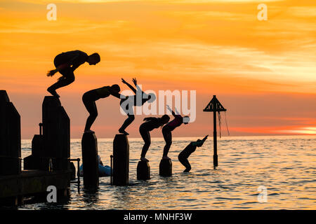 Aberystwyth Wales UK, Donnerstag, 17. Mai 2018 Deutschland Wetter: Bei Sonnenuntergang am Ende einer glorreichen Tag der warmen Frühlingssonne, eine Gruppe von Studenten sind wie Sie tauchen und springen Sie in das klare Wasser aus dem hölzernen Pier in Aberystwyth an der Westküste von Wales Foto © Keith Morris/Alamy Leben Nachrichten Silhouette Stockfoto