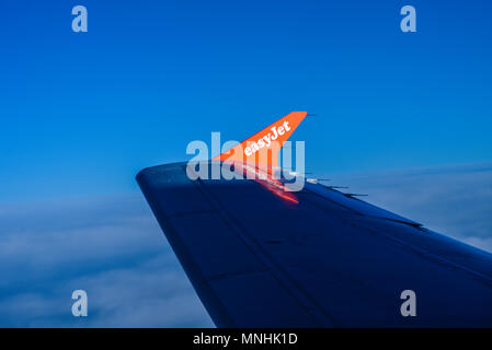 EasyJet-Schriftzug auf der Winglet mit Flügelspitze im Jet-Flugzeug bei Sonnenaufgang. Flügel im Schatten. Über Wolken im blauen Himmel. Fluggesellschaft, Flugzeug Stockfoto