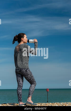 Sportliche Frau, die durch das Meer ausruhen und trinken aus einem Sport Trinkflasche