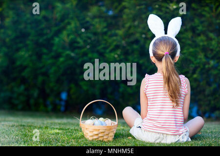 Rückansicht eines kleinen Mädchens tragen Häschenohren mit einem Korb von bunten Ostereier im Freien auf Frühling Stockfoto