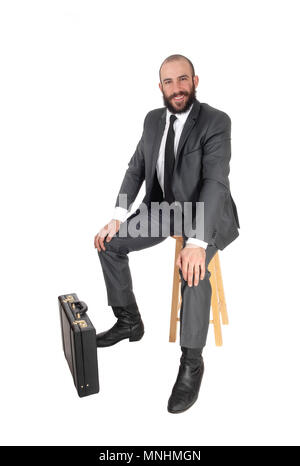 Ein junger gut aussehender Geschäftsmann in Anzug und sitzt auf einem Bar Stuhl mit seinem Aktenkoffer Krawatte, bei weißem Hintergrund Stockfoto