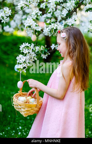 Adorable kleine Mädchen spielen mit Ostereier in einem blühenden Garten Frühling Stockfoto