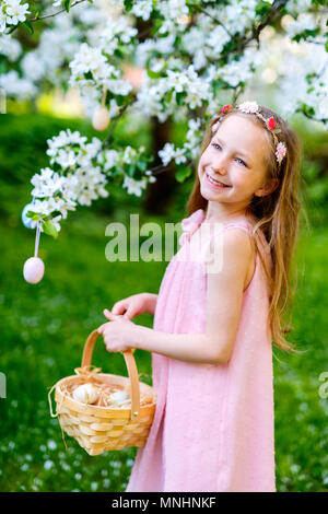 Adorable kleine Mädchen spielen mit Ostereier in einem blühenden Garten Frühling Stockfoto