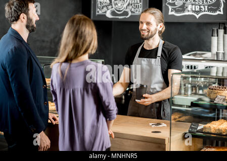 Junges Paar kaufen Kaffee stehen mit den stattlichen Barista in der modernen Coffee Shop Stockfoto