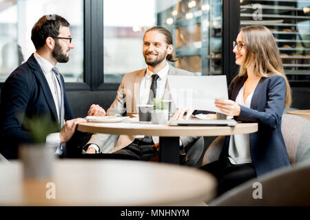 Drei Geschäftsleute arbeiten mit Dokumenten zusammen sitzen während der Kaffeepause in der modernen Cafe innen Stockfoto