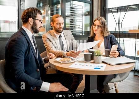 Drei Geschäftsleute arbeiten mit Dokumenten zusammen sitzen während der Kaffeepause in der modernen Cafe innen Stockfoto